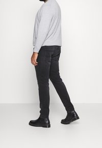 Šedá mikina s dlouhým rukávem, černé slim-fit džíny a černé chelsea boty. Hladká textura s jednoduchým, minimalistickým designem.