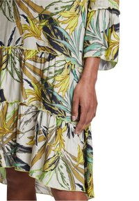 Robe à motif floral avec des volants superposés, présentant des couleurs jaune, verte et bleu foncé. Fabriquée en tissu léger, avec un design à manches évasées.