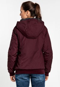 Maroon hooded jacket with ribbed cuffs and hem, featuring a smooth exterior and a quilted inner lining, viewed from the back.