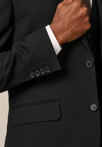Schwarze Anzugjacke aus strukturiertem Stoff, vier schwarze Knopfakzente am Ärmel und eine taillierte Tasche an der Seite.