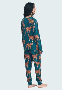 Completo pigiama color teal con motivo di tigri arancioni, composto da una maglietta a maniche lunghe e pantaloni abbinati che mostrano lo stesso design. Tessuto morbido.