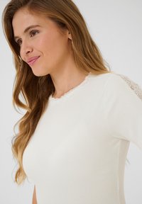 Lichtcrème geribbelde top met korte mouwen, voorzien van een geschulpte kantaccent op de schouders, een soepele textuur en een aansluitend ontwerp.