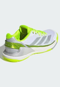 White athletic shoe with neon green accents, silver detailing, and a textured mesh upper. Features a cushioned sole and reinforced heel.