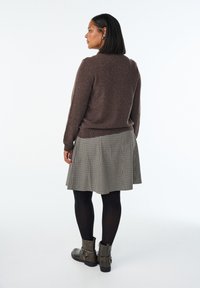 Brun strikket sweater, plisseret ternet nederdel, sorte strømpebukser og grå ankelstøvler med stropper, vist fra bagsiden mod en hvid baggrund.