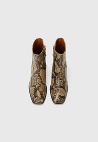 Bottines à talon moyen avec un motif imprimé serpent beige et noir, présentant un design structuré, un bout pointu et des fermetures éclair sur le côté.