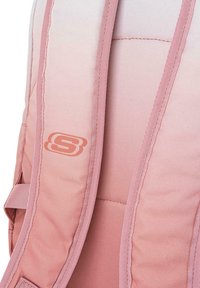 Mochila de tela rosa con diseño ombre, correas acolchadas y detalle de logo. La textura parece suave con costuras visibles y correa lateral ajustable.