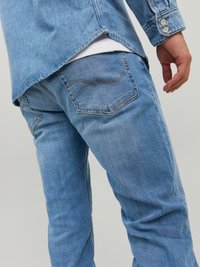 Vaqueros de mezclilla de color azul claro con un corte ligeramente ajustado, que presentan un bolsillo trasero con un detalle de costura y una superficie texturizada.