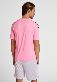 Camisa deportiva rosa de mangas cortas, con textura suave, acentos negros en los hombros, acompañada de pantalones cortos gris claro.