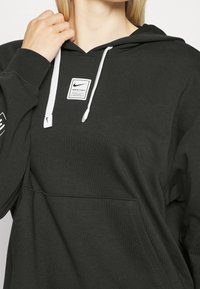 Musta huppari pehmeästä kankaasta, jossa on etutasku, valkoiset nyörit ja pieni logopatch rintakehässä.