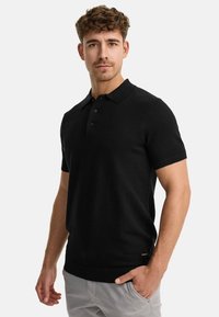 Black short-sleeve polo shirt with a textured knit, three-button placket, and ribbed collar and hem, paired with light-colored pants.