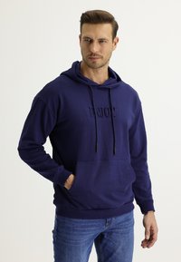 Felpa con cappuccio in cotone blu navy con cordoncini, tasca frontale a marsupio e testo in rilievo "ENJOY" sul petto. Maniche lunghe, vestibilità comoda.