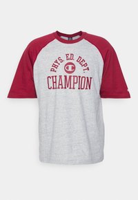 Camiseta de manga corta gris con mangas raglán en color burdeos. Presenta el texto "DEPTO. DE EDUCACIÓN FÍSICA CAMPEÓN" en letras burdeos en negrita y un detalle del logo.