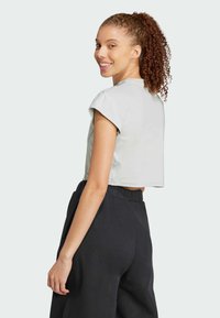 Lühendatud hall tops rullitud varrukatega koos lõtvade mustade pükstega. Sile kangas, mugav lõige ja elastne vöökoht.