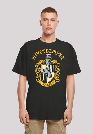Black T-shirt featuring the Hufflepuff crest in yellow and gray, with intricate gold accents and a badger emblem on a shield background.