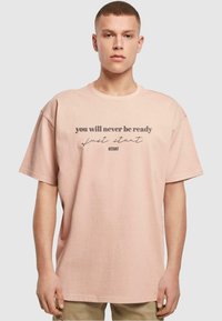 Lyserød oversized t-shirt med korte ærmer. Forsiden har sort tekst: "du vil aldrig være klar, bare start #START." Blødt materiale.