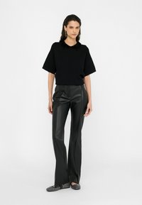Black knit top with a beaded collar, paired with high-waisted black faux leather pants and textured black flats. Simple design, no patterns.