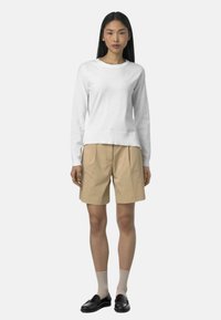 Maglione bianco a maniche lunghe con scollo e orlo a coste, abbinato a pantaloni shorts beige con pieghe e mocassini neri, indossato con calzini leggeri.