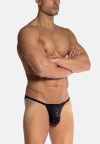 Czarny string wykonany z materiału w wzory, o półprzezroczystej fakturze, z minimalnym zakryciem i cienkim paskiem w talii.