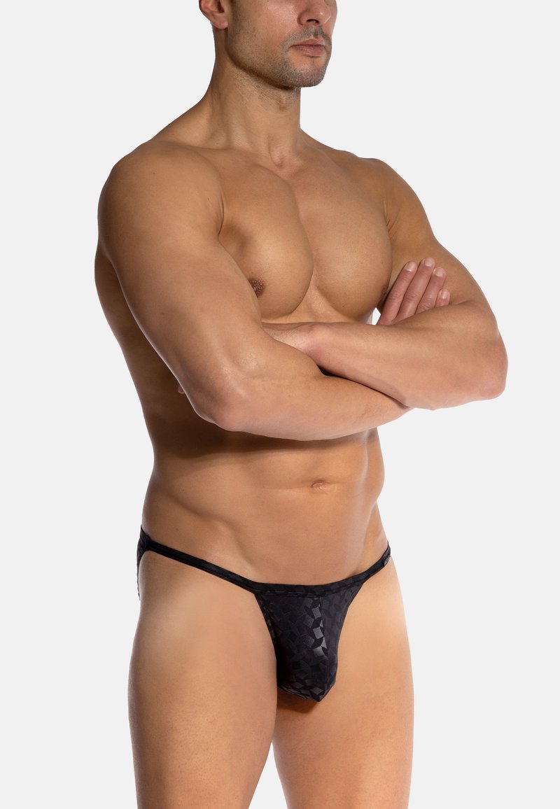 Czarny string wykonany z materiału w wzory, o półprzezroczystej fakturze, z minimalnym zakryciem i cienkim paskiem w talii.