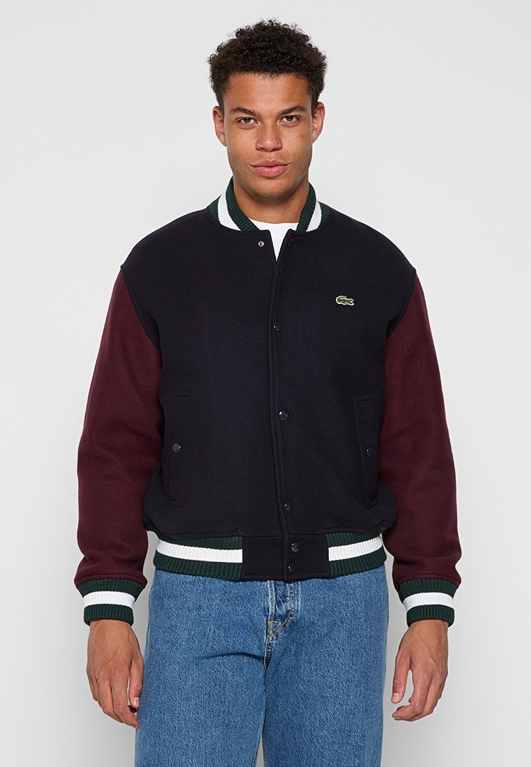 Blouson en laine mélangée bleu marine foncé avec des manches bordeaux, des poignets et un ourlet côtelés à rayures vertes et blanches, présentant un petit logo vert sur la poitrine.