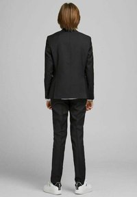 Černý oblek s upraveným sakem a úzkými kalhotami, doplněný bílými teniskami. Hladká tkanina s čistým designem a minimálním zdobením.