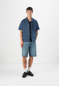 Short-sleeve denim shirt with a textured blue pattern, paired with light blue shorts, black shoes, and white socks.