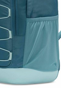 Teal-reppuosa, jossa on teksturoitu kangas, verkkosivutasku ja kestävä pohja, suunniteltu toimivuuden ja tyylin yhdistämiseksi.