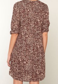 Lös passform klänning i lätt tyg med ett brunt och krämfärgat svängande blommönster, med uppvikta ärmar och rund halsringning.