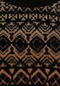 Suéter de punto con un patrón geométrico en negro y beige. El diseño incluye diamantes y líneas con una apariencia texturizada y suave.