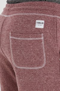 Los pantalones de chándal rojos jaspeados presentan un bolsillo trasero blanco con costuras y una etiqueta con la marca "SOLID", fabricados en un tejido suave y texturizado.