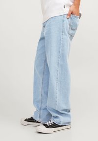 Jeans de mezclilla de pierna ancha en azul claro con un lavado ligero, que cuentan con bolsillos laterales y detalles de costura, combinados con zapatillas negras y blancas.