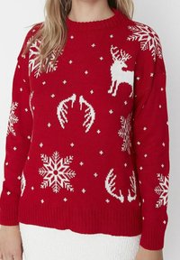 Rode gebreide trui met witte sneeuwvlokken, rendieren en geweien in een herhalend patroon. Ribbelkraag en mouwen.