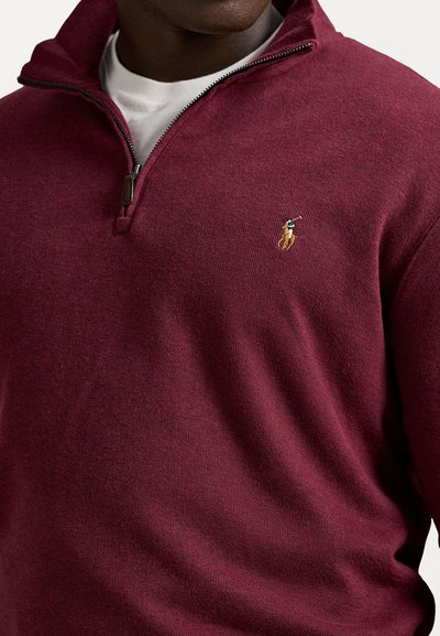 Man wearing a maroon quarter-zip sweater with a white undershirt, featuring a small embroidered polo player logo on the chest.