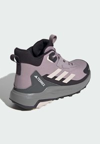 Světlé šedé turistické boty s černými akcenty, texturovaný síťovaný svršek, výrazné tři bílé pruhy a robustní podrážka pro lepší trakci.