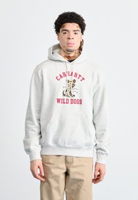 Sudadera gris con bolsillo delantero, con el texto "Carhartt Wild Dogs" y una ilustración de un perro. Tejido suave, capucha con cordón ajustable.