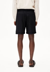 Zwarte shorts met een elastische tailleband, zij- en achterzakken, en opgerolde boorden, gecombineerd met een lichtgestreept overhemd met lange mouwen.
