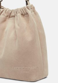 Sac à main en suède beige avec un dessus froncé, une forme structurée, un détail de logo embossé et une texture lisse. Doté de poignées courtes et plates.