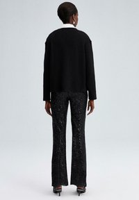 Zwart geribd sweater met een ronde halslijn. Flared zwarte pailletten broek met een franjes zoom. Hakken maken de outfit af.