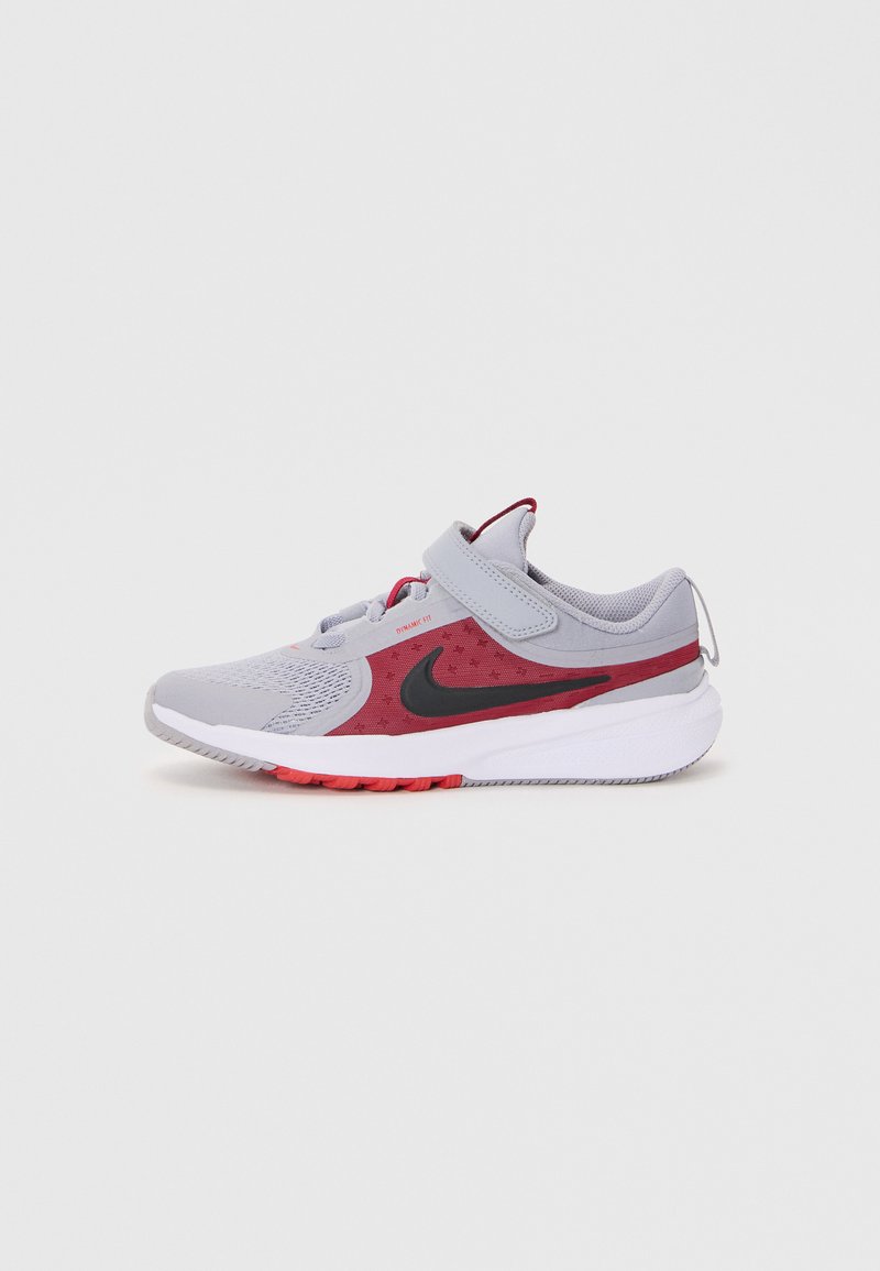 Chaussure de sport avec une tige en mesh gris agrémentée d'accents rouges, un swoosh noir de Nike, une sangle Velcro et une semelle blanche texturée avec des détails rouges.