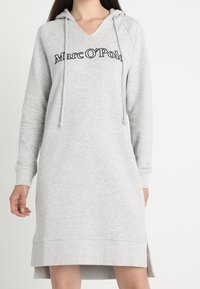 Graues Kapuzenkleid mit V-Ausschnitt, featuring "Marc O'Polo" Logo. Hergestellt aus weichem Stoff, mit seitlichen Schlitzen und gerippten Bündchen und Saum.