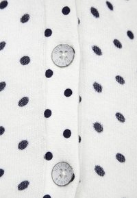 Vitt stickat tröja med blå prickar, med knappstängning där "HILFIGER DENIM" är ingraverat. Mjuk textur, avslappnad design.