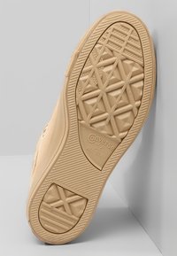 Světlé béžové tenisky Converse All Star mají podešev s geometrickým vzorem a vyraženým logem. Hladký povrch s kulatou špičkou a vyvýšeným gumovým okrajem.