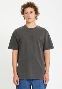 T-shirt in cotone grigio scuro con maniche corte, scollo tondo e un logo cerchiato in rilievo sul petto, abbinato a pantaloni corti in denim blu.