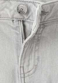 Lichtgrijze spijkerbroek met een open ritssluiting en een zilveren knoop gegraveerd met "AUTHENTIC DENIM WING."