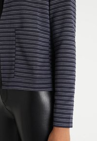 Marineblå randig jacka med en texturerad tyg, med långa ärmar och en framficka, kombinerad med glänsande svarta leggings.