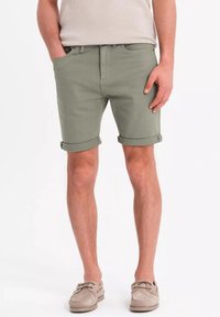 Shorts en coton verts avec des revers, dotés de poches avant et d'une taille plate. Portés avec des chaussures beiges.