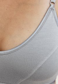 Grijze naadloze bralette met een zachte textuur, dunne verstelbare bandjes en subtiele stikdetails, met een gebogen halslijn en gladde stof.