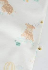 Miękka biała tkanina z jasnobrązowymi kreskówkowymi krowami, żółtymi pszczołami, turkusową konewką i subtelnymi zielonymi ilustracjami trawy.