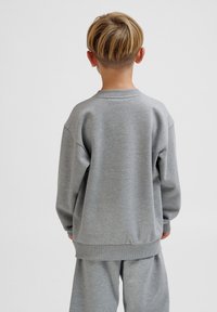 Grauer Pullover aus weichem Stoff, mit einem gerippten Halsausschnitt, überschnittenen Schultern und einer lässigen Passform. Die Rückansicht zeigt minimale Details.