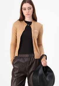 Beige kasjmir cardigan med knaplukning og "2ND DAY" broderet på brystet. Sammen med sort tætsiddende top og løse brune lærbukser. Sort håndtaske.